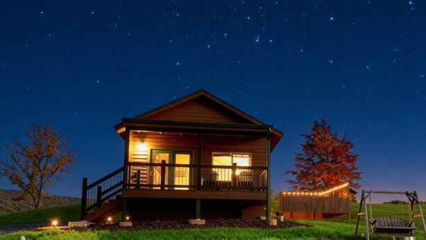 A wooden cabin with a balcony, illuminated windows, and a starry night sky.
