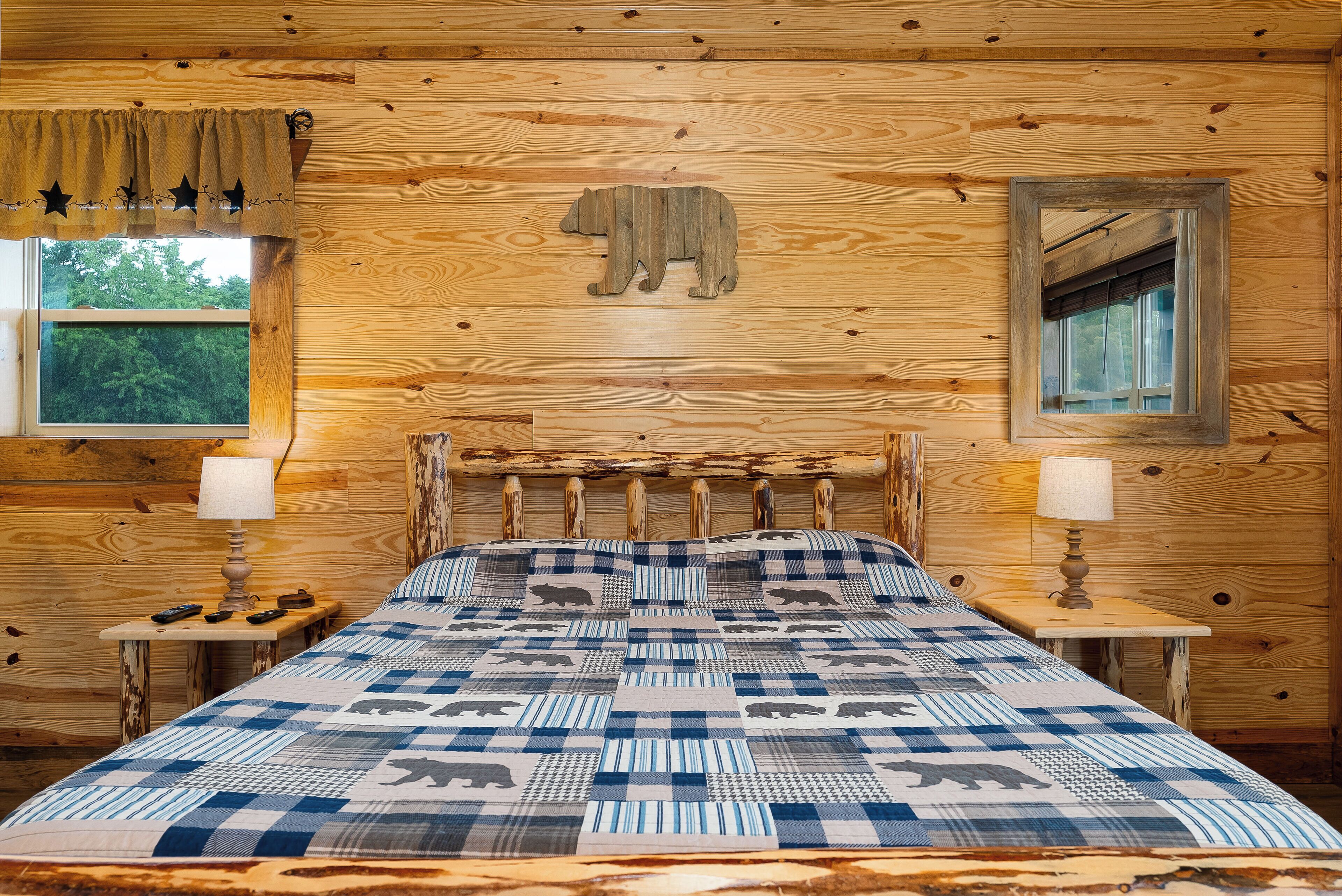 Une pièce de cabane en bois comprenant un lit, deux tables de chevet, une fenêtre et une décoration murale en forme d’ours.