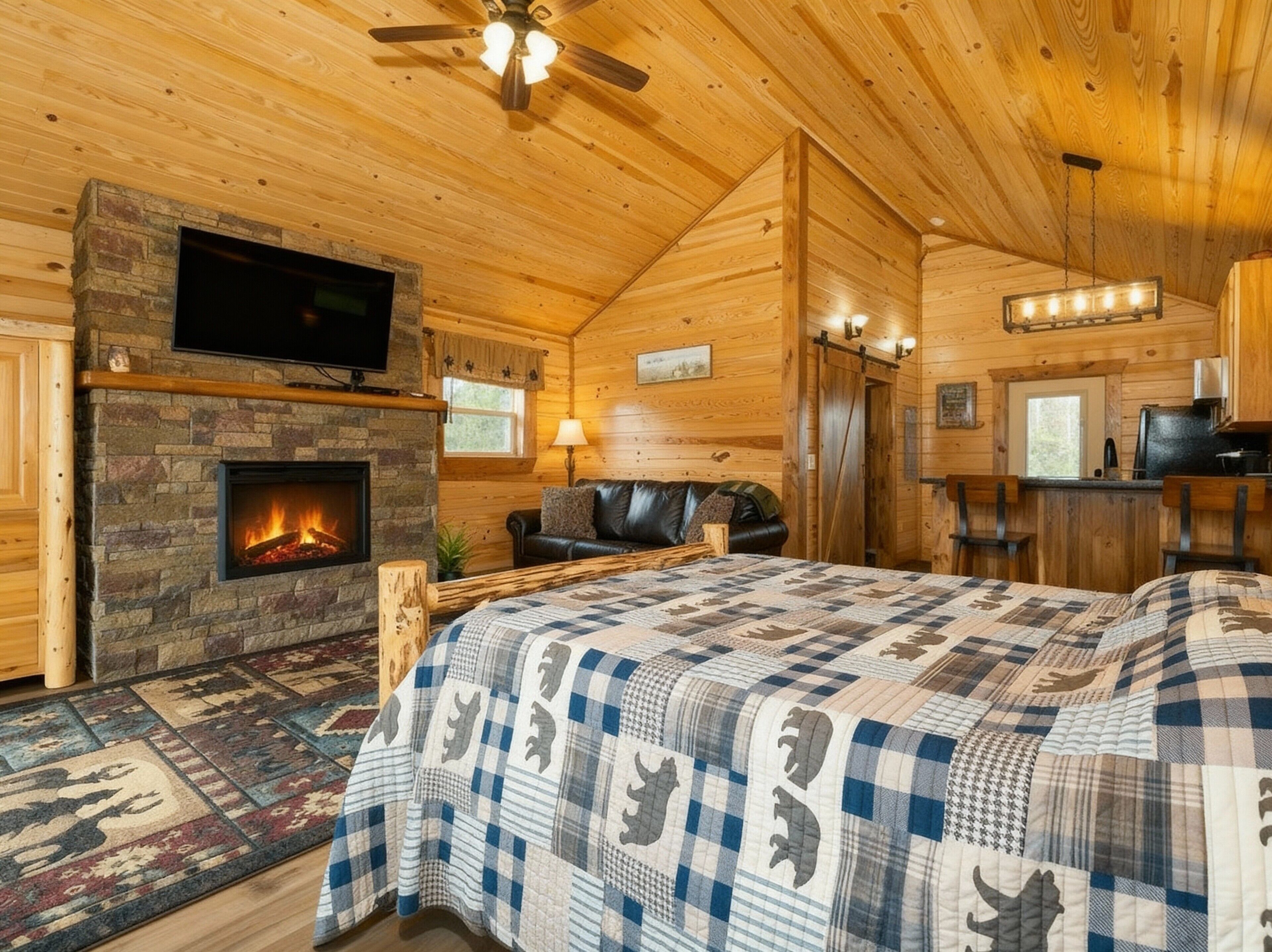 L’intérieur d’un chalet confortable en bois, avec une cheminée, un grand lit, une télévision et un coin repas.