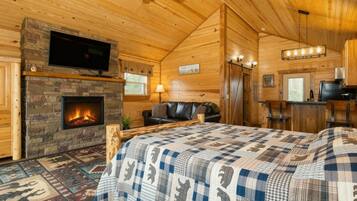 L’intérieur d’un chalet confortable en bois, avec une cheminée, un grand lit, une télévision et un coin repas.