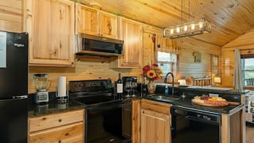 Une cuisine rustique aménagée dans une cabane en bois, comprenant un réfrigérateur, une cuisinière, un four à micro-ondes et des placards en bois.