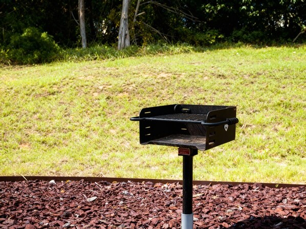 Una parrilla de barbacoa en un poste, en un área con césped y acolchado.