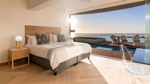 Une chambre avec un grand lit, une table de chevet, une table en verre et une vue sur la mer.