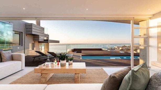 Un salon moderne doté d’une grande fenêtre donnant sur une piscine et offrant une vue sur l’océan.