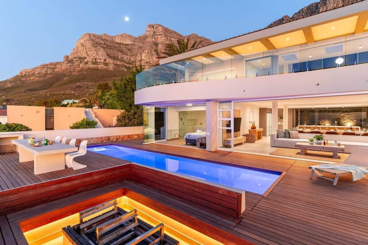 Une maison moderne dotée d’une grande piscine, d’un espace salon extérieur et offrant une vue sur les montagnes.