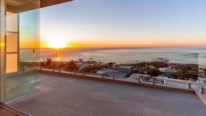 Un balcon doté d’une balustrade en verre, d’où l’on peut admirer un coucher de soleil sur l’océan.