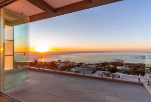 A balcony with a glass railing overlooking a sunset over the ocean. - The Summit Camps Bay - Luxury Villa | Views | Pool (Cape Town)