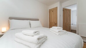 Een opgemaakt bed met gevouwen witte handdoeken, een bedlampje en houten deuren op de achtergrond.