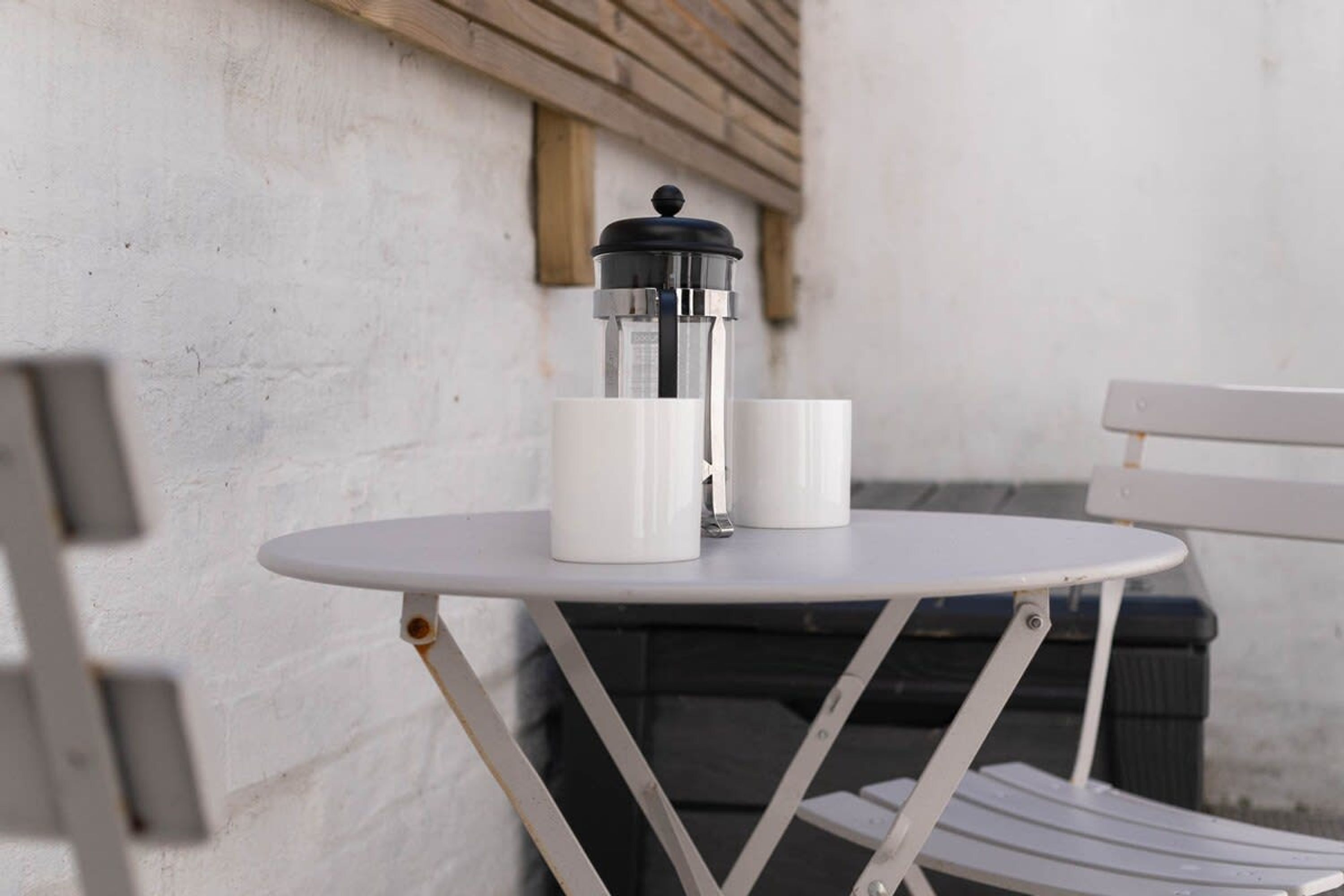 Une table en métal blanc, avec deux tasses blanches et une cafetière à piston noire.