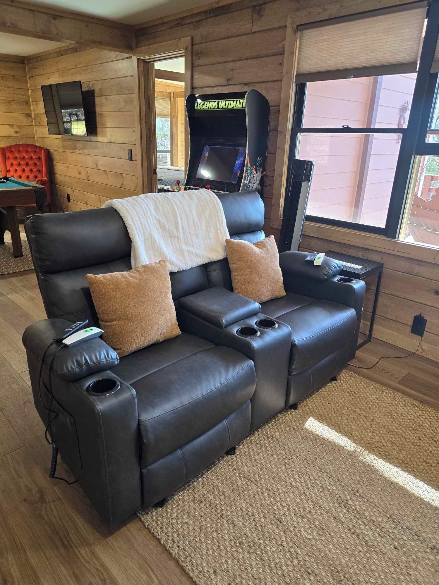 Un canapé en cuir noir, accompagné de deux tables d’appoint et d’une couverture, une table de billard et un téléviseur, le tout dans une pièce au décor en bois.