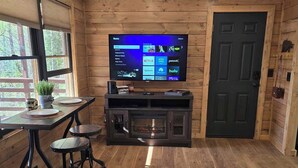 Una habitación acogedora con paredes de madera, un televisor de pantalla plana grande montado en la pared, una mesa de comedor con sillas y una puerta decorada con un oso.