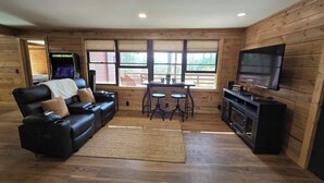 Una sala de estar acogedora con un sofá de cuero, televisor, chimenea y un amplio ventanal con vistas al exterior.
