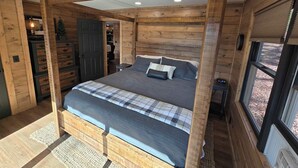 Un dormitorio tipo cabaña de madera con una cama, una mesita de noche y una ventana.