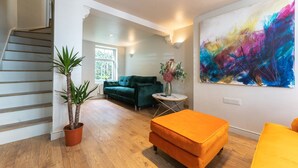 Uma sala de estar moderna com escada, um sofá verde, um banquinho laranja e uma pintura abstrata colorida.