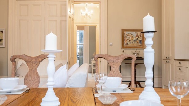 Un coin repas avec une table en bois dressée pour quatre personnes, des chandeliers blancs et un tableau accroché au mur.