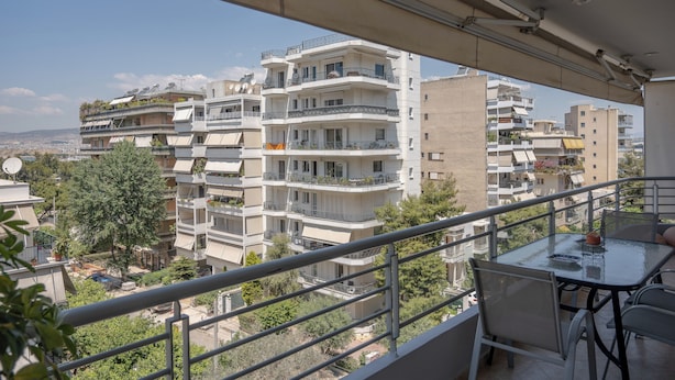 Ein Balkon mit Tisch und Stühlen, der auf einen Wohnbereich mit mehrstöckigen Gebäuden und Grünflächen blickt.