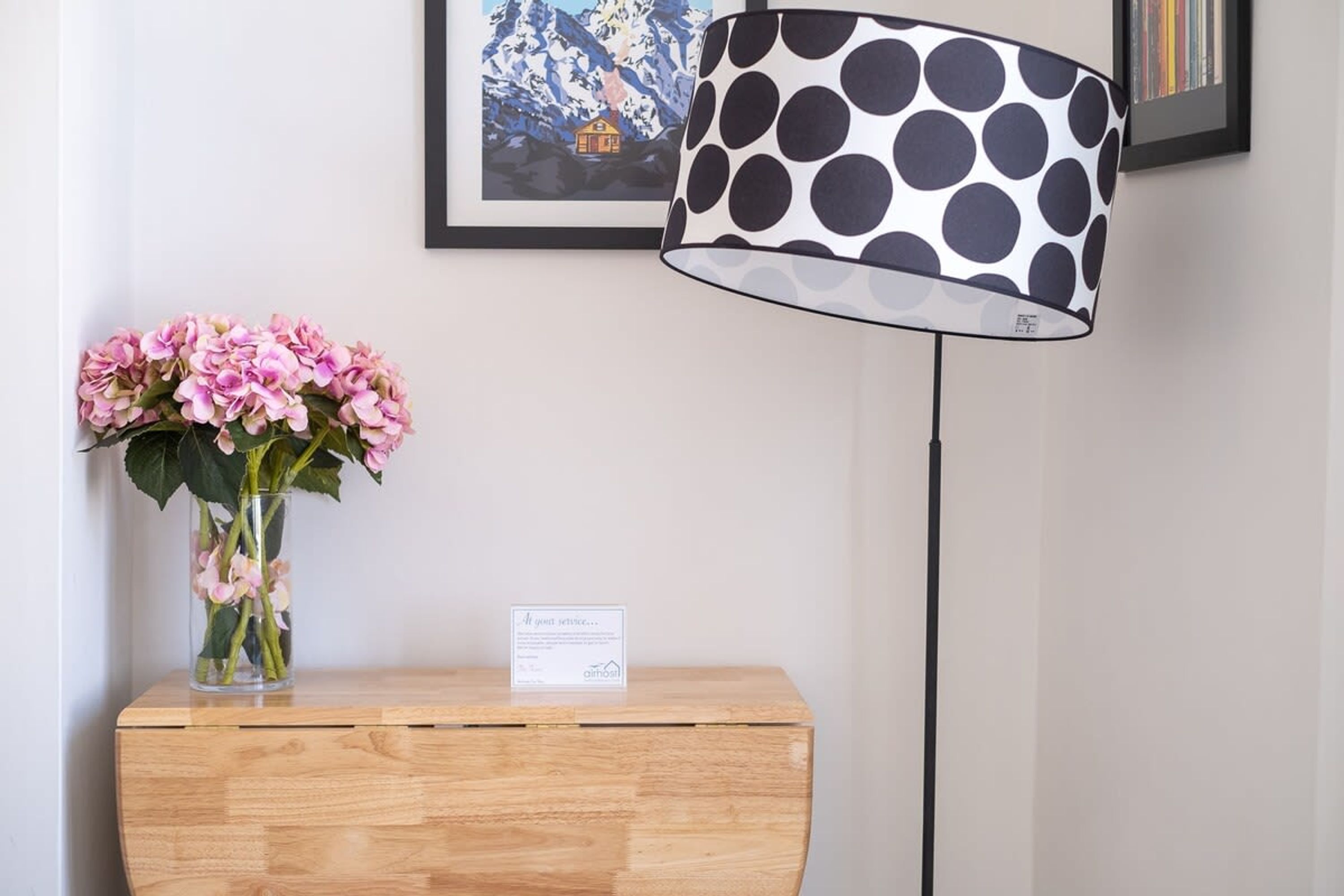 Un mostrador de recepción de madera con un jarrón de flores rosas y una lámpara a lunares negros y blancos.