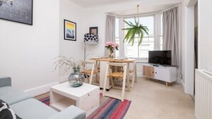 A modern living room with a sofa, a coffee table, a dining table with chairs, a TV, and a potted plant. - Host Stay Guildford Apartment (Brighton)