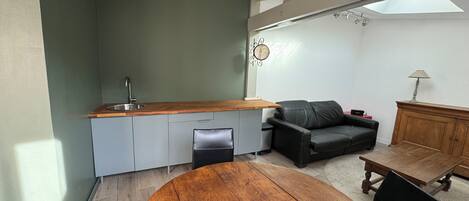A compact living space with a kitchen area, a dining table, a sofa, and a lamp.