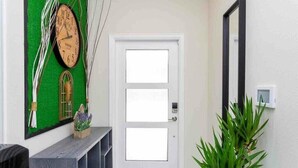 A hallway with a white door, a green wall with a clock, and a plant. - Go!#01 - CHAMPIONS GATE (Kissimmee)