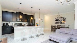 A modern kitchen with dark cabinets, a central island with bar stools, and pendant lighting. - Go!#01 - CHAMPIONS GATE (Kissimmee)