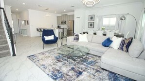 A modern living room with a glass coffee table, a white sofa, and a blue armchair. - Go!#04 - CHAMPIONS GATE (Kissimmee)