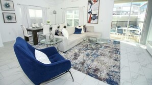 A modern living room with a sofa, armchairs, a glass coffee table, and a dining area with a table and chairs. - Go!#04 - CHAMPIONS GATE (Kissimmee)