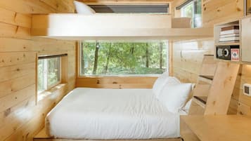 Un dormitorio de cabaña de madera con literas, ventanas amplias y vistas al bosque.