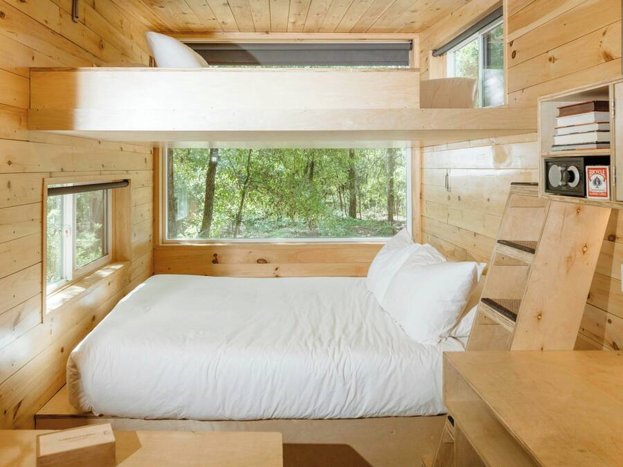 Un dormitorio de cabaña de madera con literas, ventanas amplias y vistas al bosque.