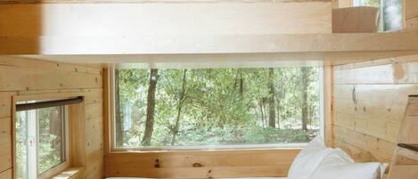 A wooden cabin with a bunk bed, a window with a view of trees, and a small desk.