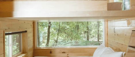 L’intérieur d’un chalet en bois, avec un lit superposé, une fenêtre donnant sur les arbres et un petit bureau.