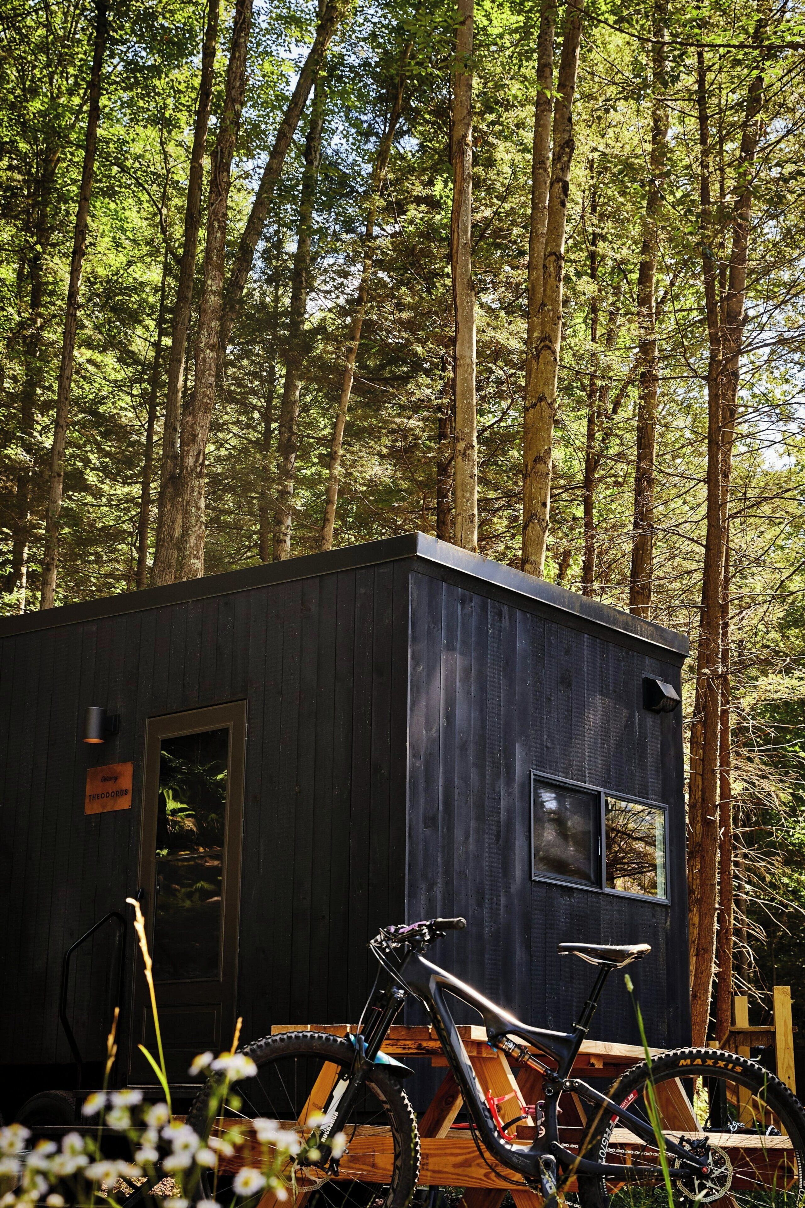 Una piccola cabina con esterno scuro, una finestra e una porta. Una bicicletta è parcheggiata davanti alla cabina.