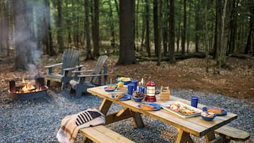 Un'area picnic con un braciere, un tavolo di legno e panche in una foresta.