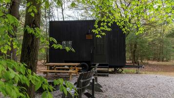 A small, black RV with a picnic table and a single chair in a wooded area.