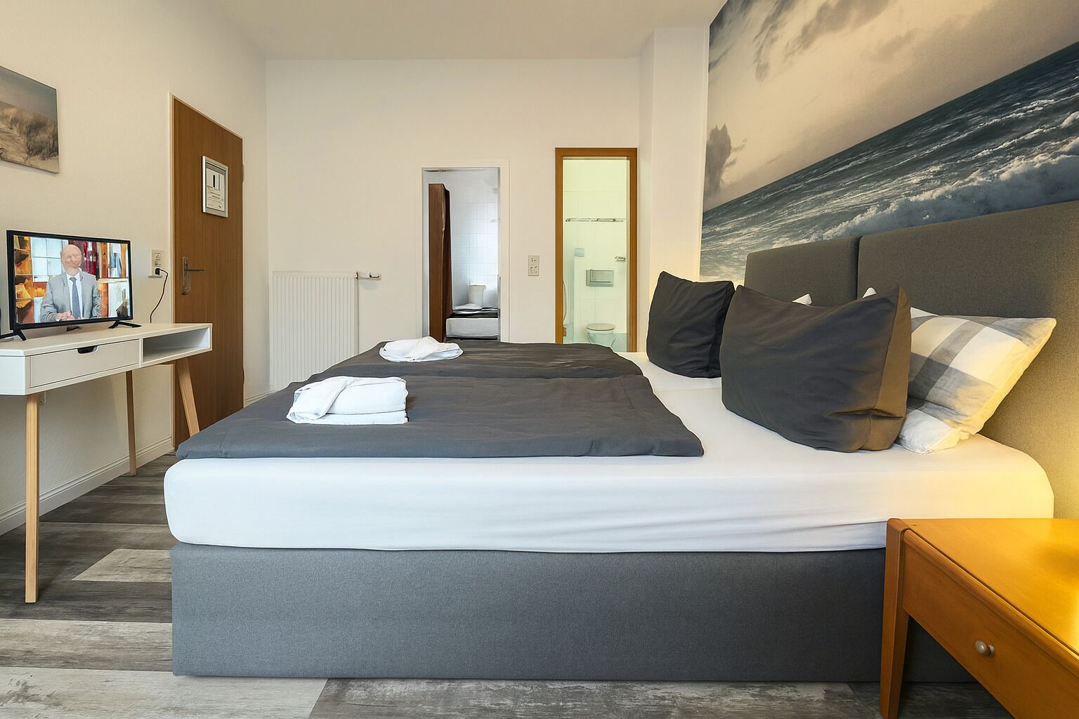 Habitación de hotel con una cama grande, un escritorio con una computadora y un cuadro del océano.