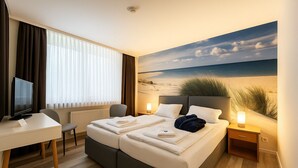 Ein Hotelzimmer mit einem Bett, einem Schreibtisch, einem Sessel, einem Fernseher und einem Bild mit einer Strandansicht.
