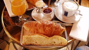 Ein Frühstücksbrett mit Croissants, Brot, Orangensaft, Kaffee und Marmelade.