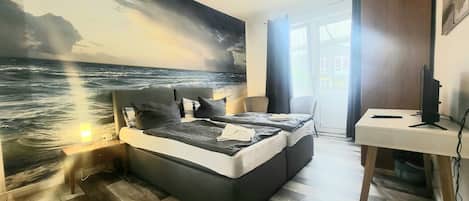 A bedroom with a bed, a desk, and a large ocean mural on the wall.