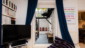 Un salón con televisor, estantería y vistas a un balcón.