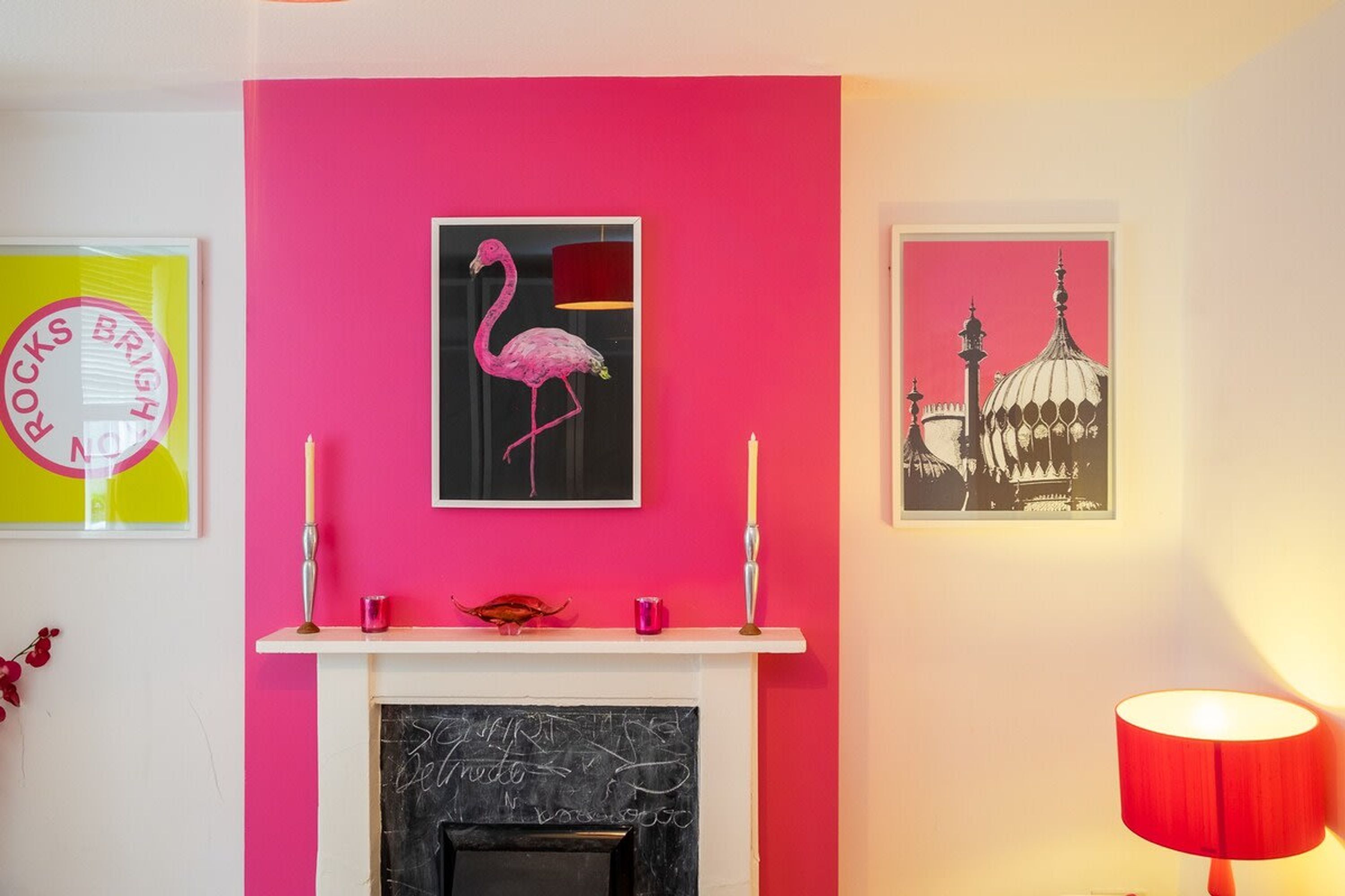 A room with a pink wall, a fireplace, and two framed pictures.
