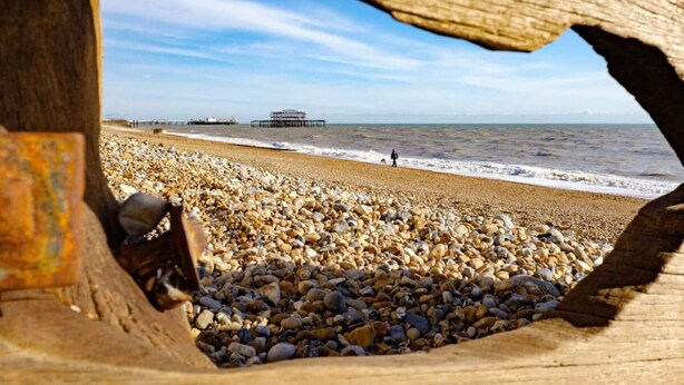 Una playa con piedras y un muelle al fondo.