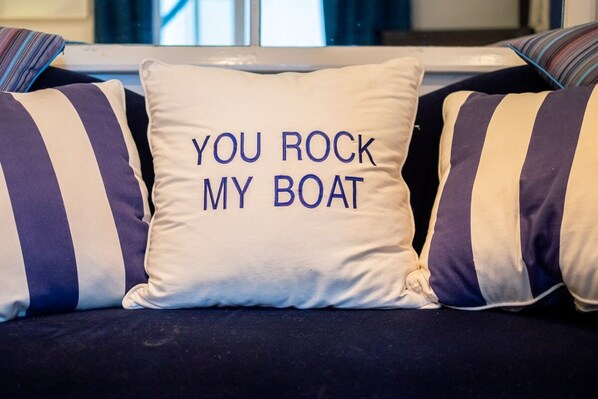 Un sofá con almohadones a rayas y un almohadón con el texto 'YOU ROCK MY BOAT'.