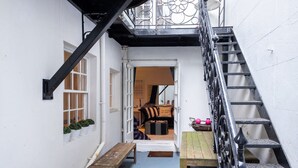 Un estrecho callejón con un banco de madera, una pequeña mesa y una escalera que conduce a un nivel superior.