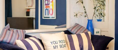 A dark blue sofa with striped pillows, a framed picture with colorful text, and a vase with white flowers.