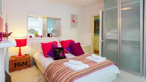 Un dormitorio con cama, mesita de noche con lámpara, espejo, ventana, puerta y armario.