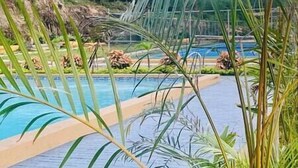 Ein Schwimmbecken mit gepflastertem Deck, umgeben von Grün und einer felsigen Landschaft.