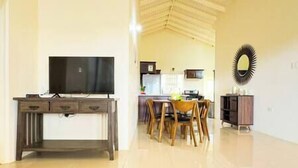 A spacious living area with a flat-screen TV on a wooden cabinet, a dining table with chairs, and a kitchen in the background. - Girls Trip ! Stay, Play and Eat $29PP (Falmouth)