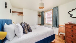 Ein Schlafzimmer mit einem Bett, einer Kommode, einem Kleiderhaken, einem Fenster mit Vorhängen und einer Deckenleuchte.