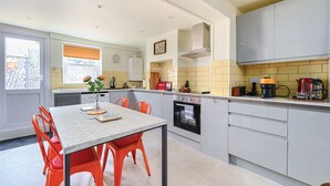 Eine moderne Küche mit grauen Schränken, einem eingebauten Backofen und einem Essbereich mit Tisch und orangefarbenen Stühlen.