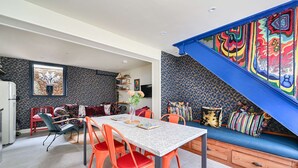 Ein Essbereich mit Tisch und Stühlen, eine Couch mit Kissen und ein farbenfrohes Wandbild.